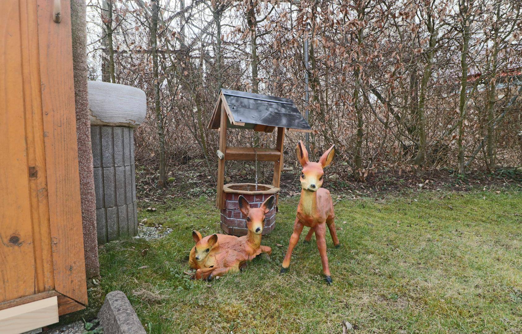 Gartendekoration mit Rehkitzfiguren und einem Zierbrunnen in einem grünen Garten.
