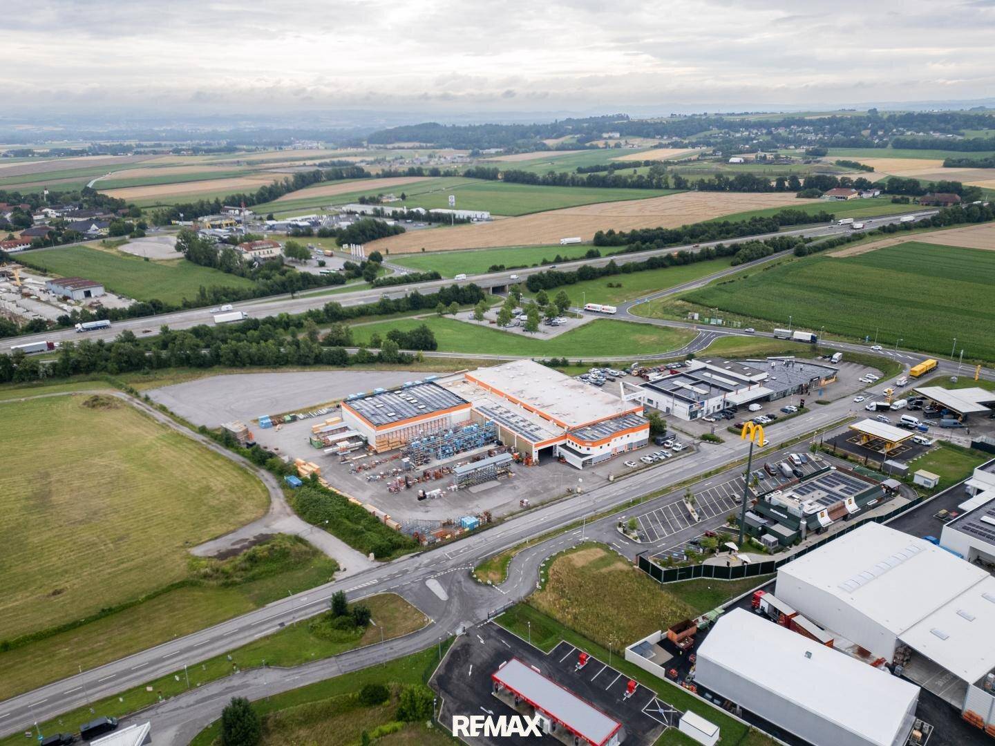 Weitläufige Luftaufnahme eines Gewerbegebiets mit Gebäuden, Parkplätzen und einer Autobahn in ländlicher Umgebung.
