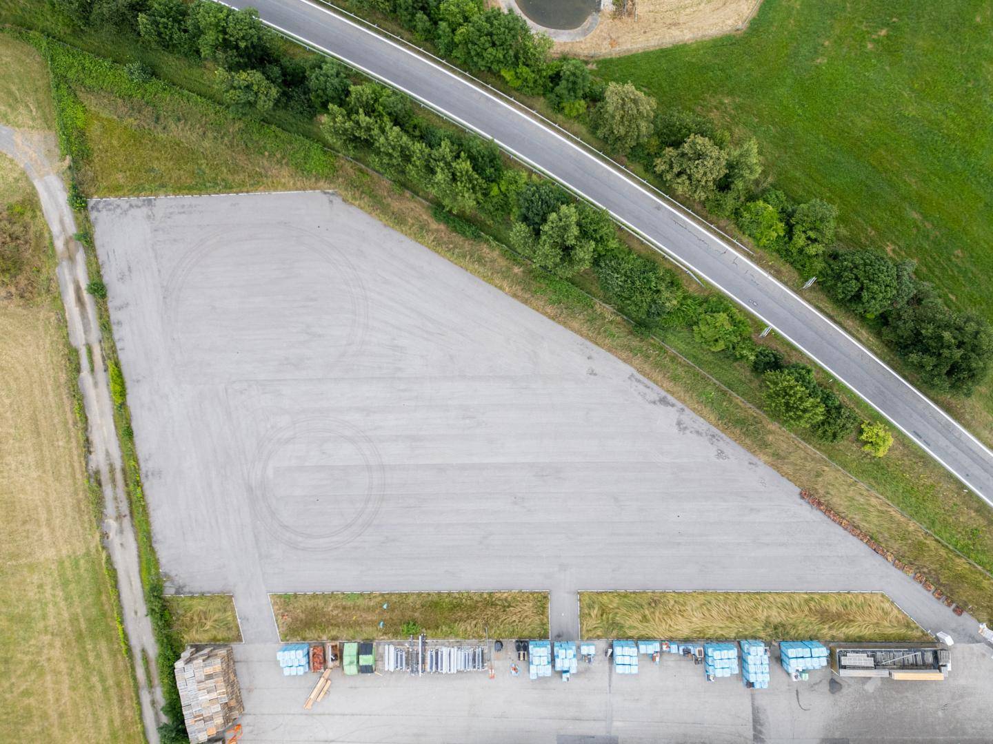 Luftaufnahme einer Autobahn mit angrenzenden Feldern und einer großen, dreieckigen Freifläche mit gelagerten Materialien.