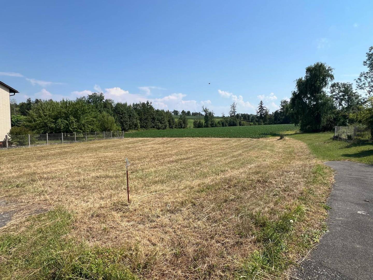 Großes Grundstück mit trockenem Gras, umgeben von Feldern und einem angrenzenden Gebäude.