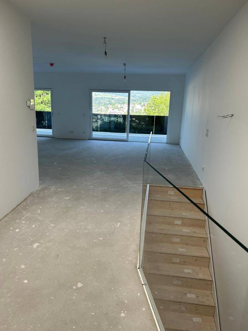 Geräumiger Flur im Rohbau mit moderner Glastreppe und weitem Blick durch die Schiebetüren.