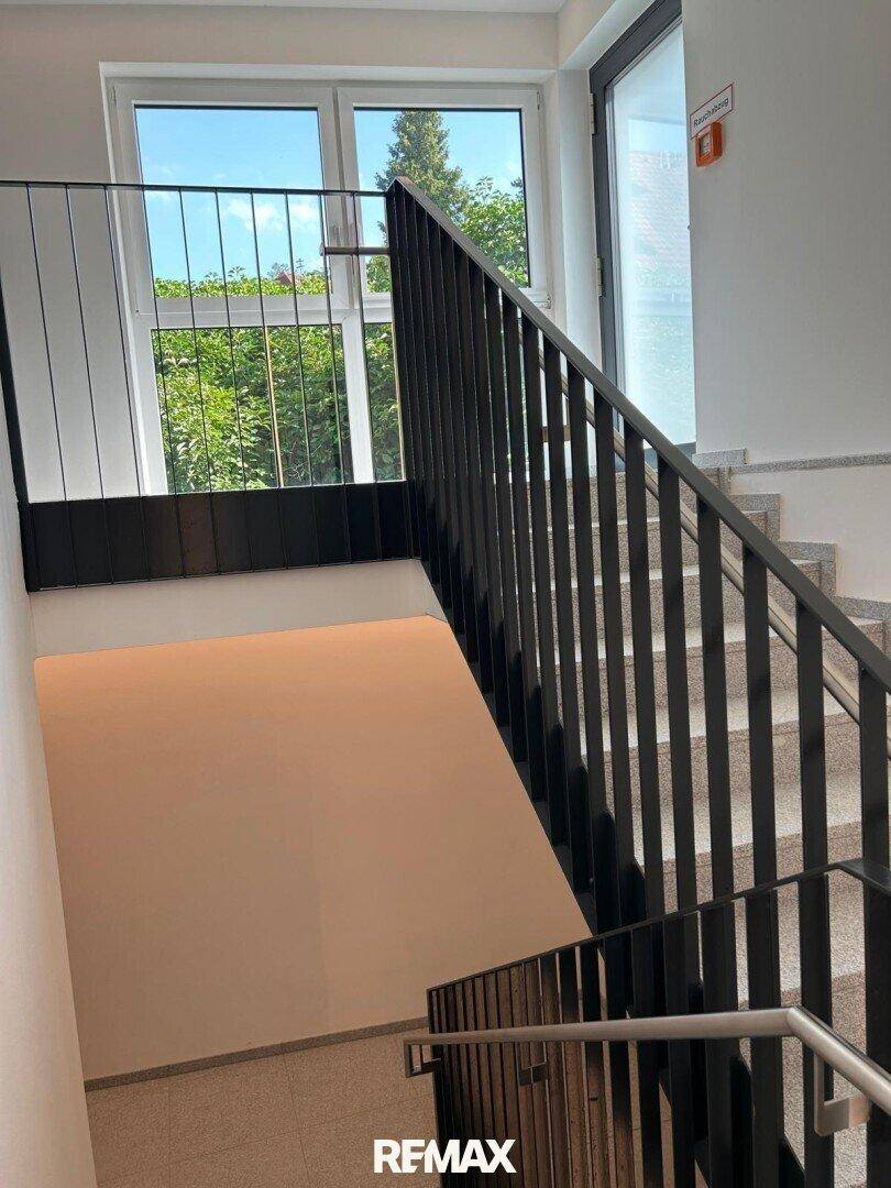 Modernes Treppenhaus mit Steinstufen, schwarzem Geländer und großem Fenster für Tageslicht.