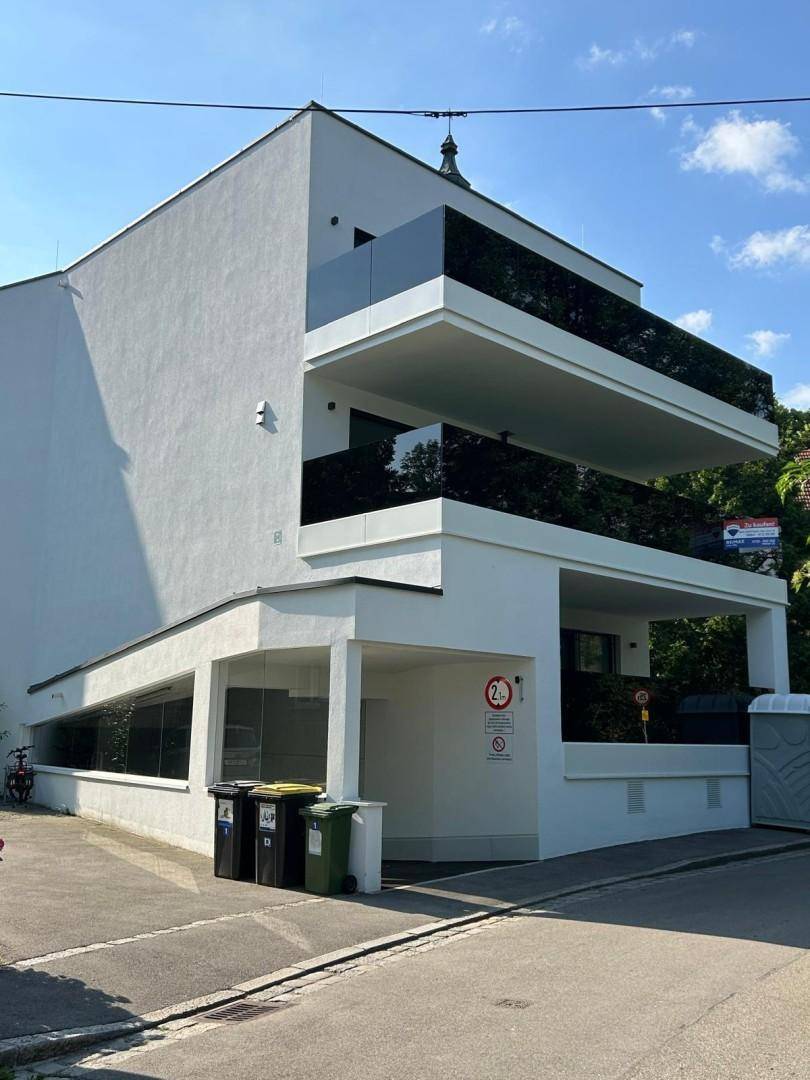 Moderne weiße Fassade eines Wohngebäudes mit schwarzen Glasbalkonen und klaren Linien.