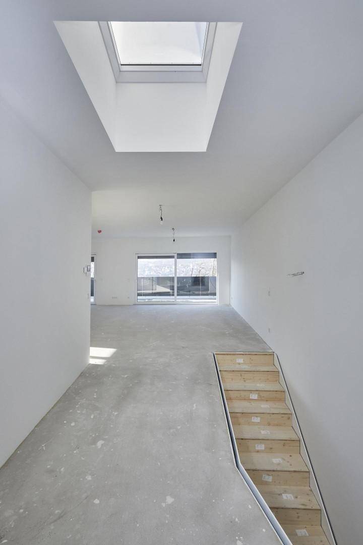 Heller Flur im Rohbau mit einer Treppe, einem Oberlicht und großen Fenstern am Ende des Raumes.