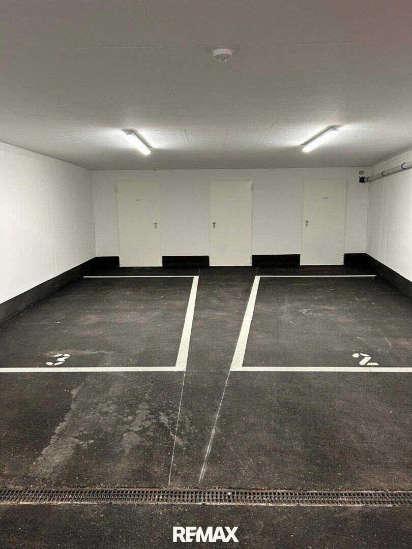 Tiefgarage mit markierten Stellplätzen und hellen Deckenleuchten.