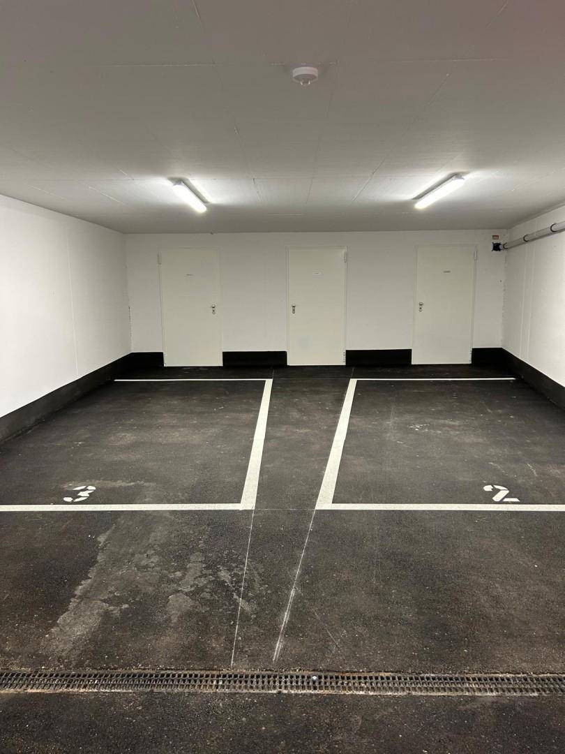 Saubere Tiefgarage mit markierten Stellplätzen und Zugangstüren, gut beleuchtet.