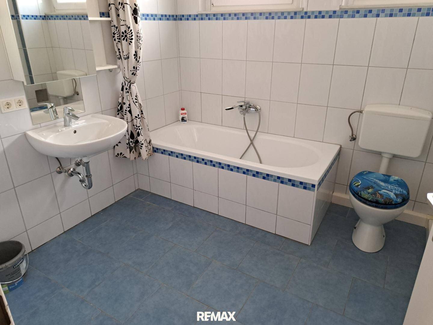 Badezimmer mit Badewanne, Waschbecken und WC, gefliest in Weiß und Blau.