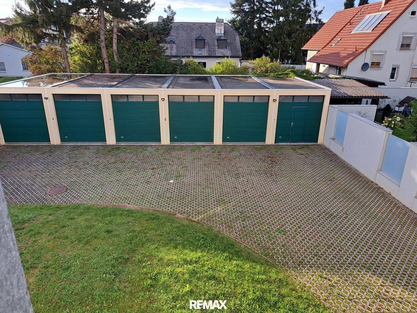 Reihe von Garagen mit grünen Toren und einem gepflasterten Parkplatzbereich.