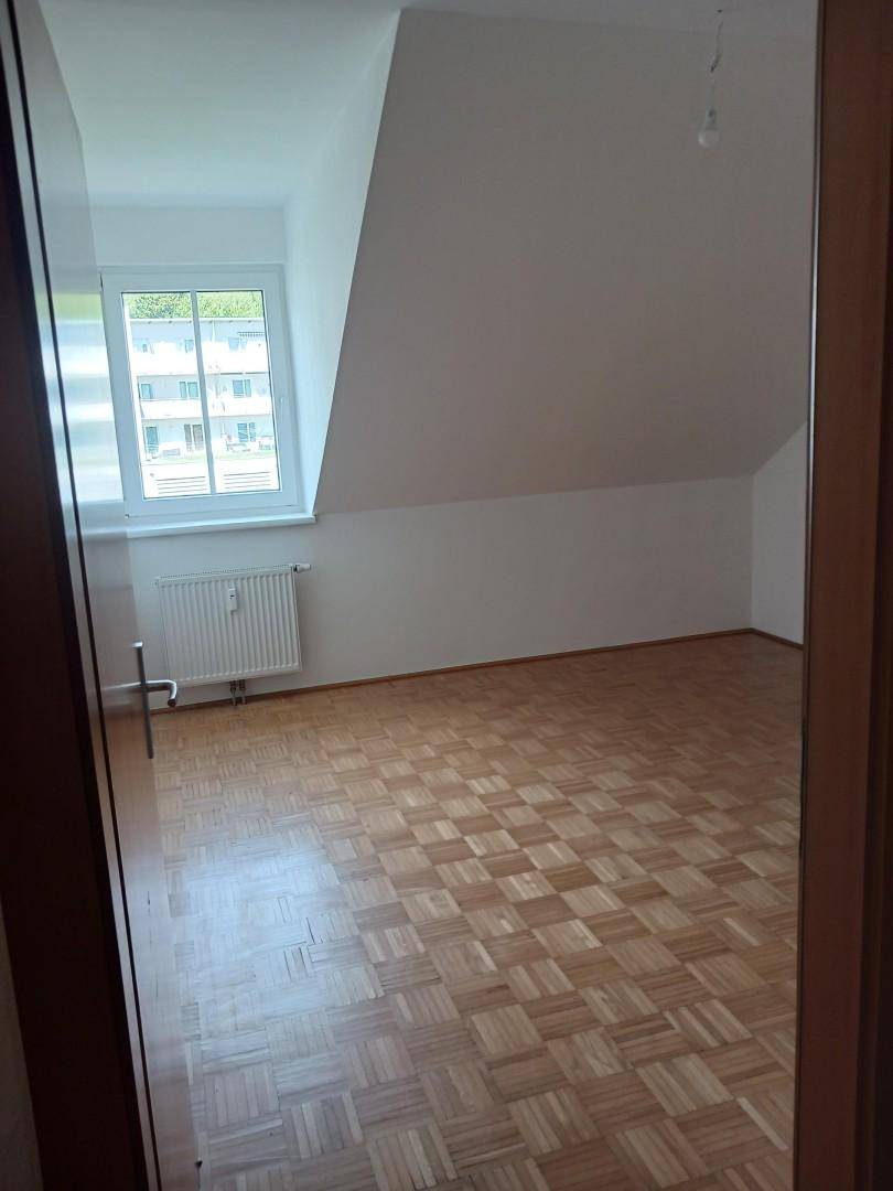 Helles Schlafzimmer mit Parkettboden, Dachschräge und großem Fenster für viel Tageslicht.