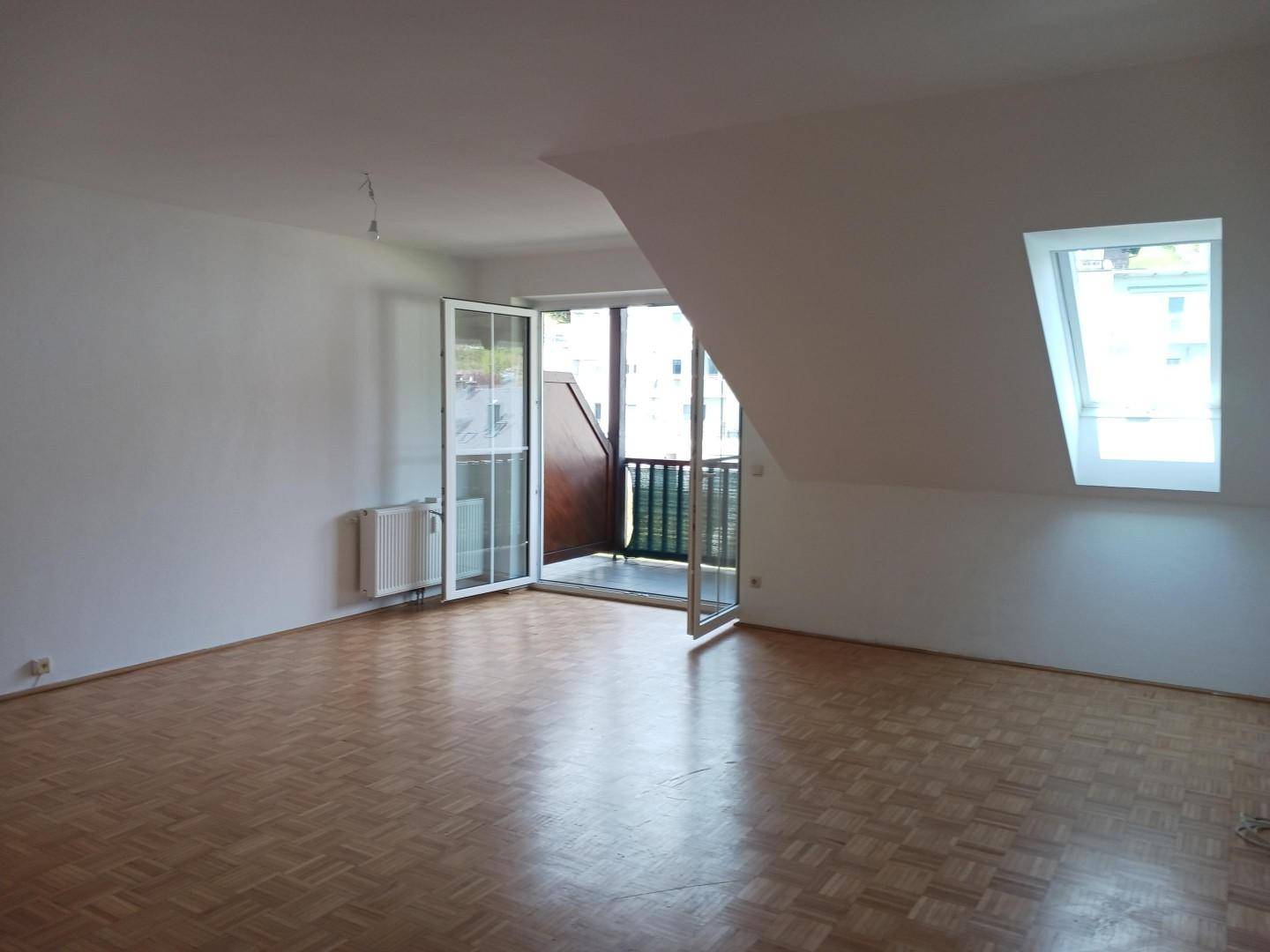 Helles Zimmer mit Parkettboden, Dachschräge und offenem Zugang zum Balkon sowie Dachfenster.