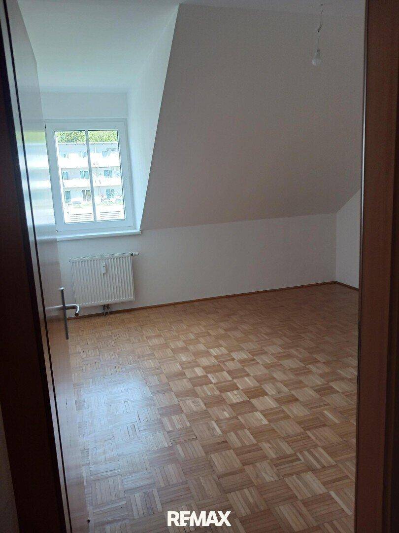 Gemütliches Zimmer mit Parkettboden, Dachschräge und einem Fenster für Tageslicht.