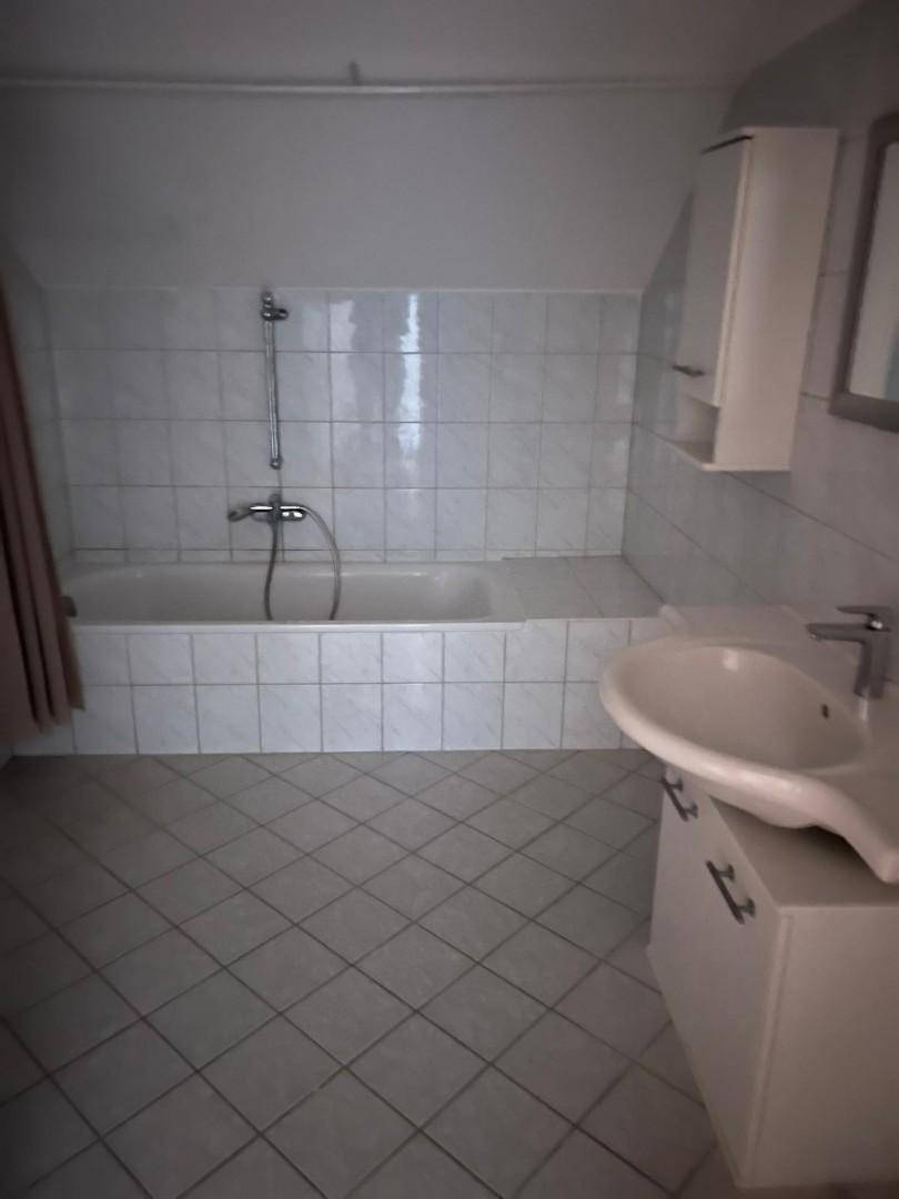 Badezimmer mit weiß gefliestem Boden und Wänden, Badewanne und Dachschräge.