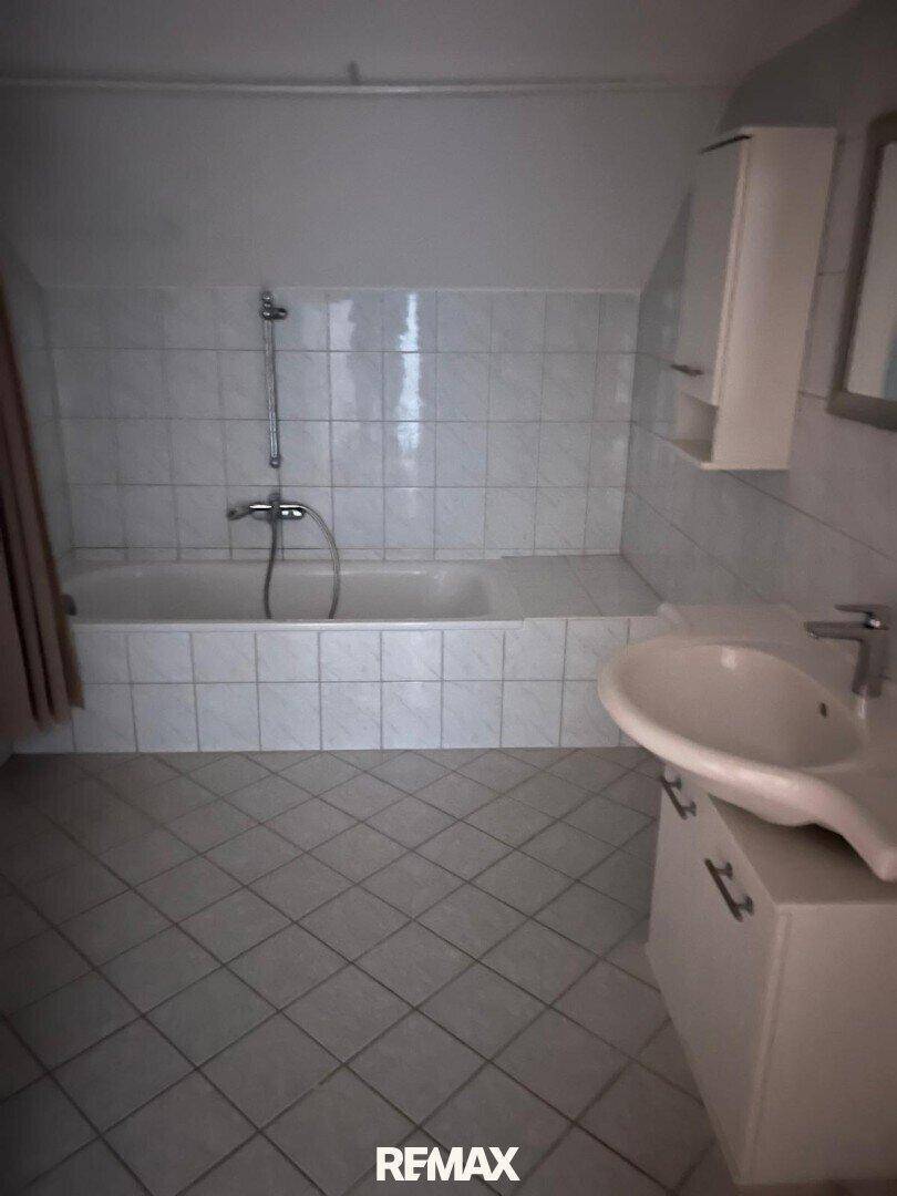 Badezimmer mit weißen Fliesen, eingebauter Badewanne und Waschbeckenunterschrank.