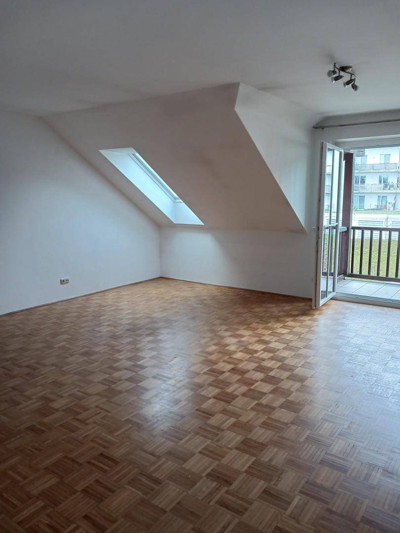 Lichtdurchfluteter Raum mit Parkett, Dachschräge, Balkonzugang und zwei Dachfenstern für viel Tageslicht.