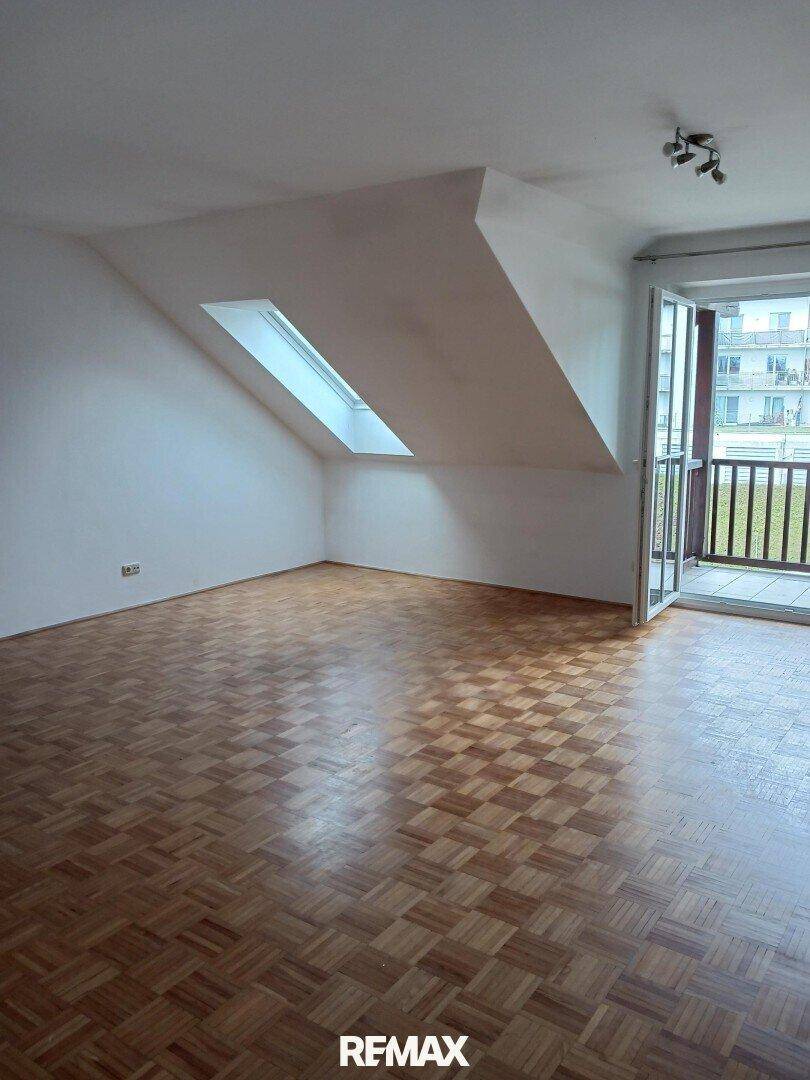 Lichtdurchfluteter Wohnraum mit Parkettboden, Dachfenstern und Balkonzugang.
