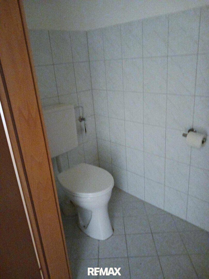 Kleines WC mit weißen Fliesen an Wänden und Boden, ausgestattet mit einer Toilette.