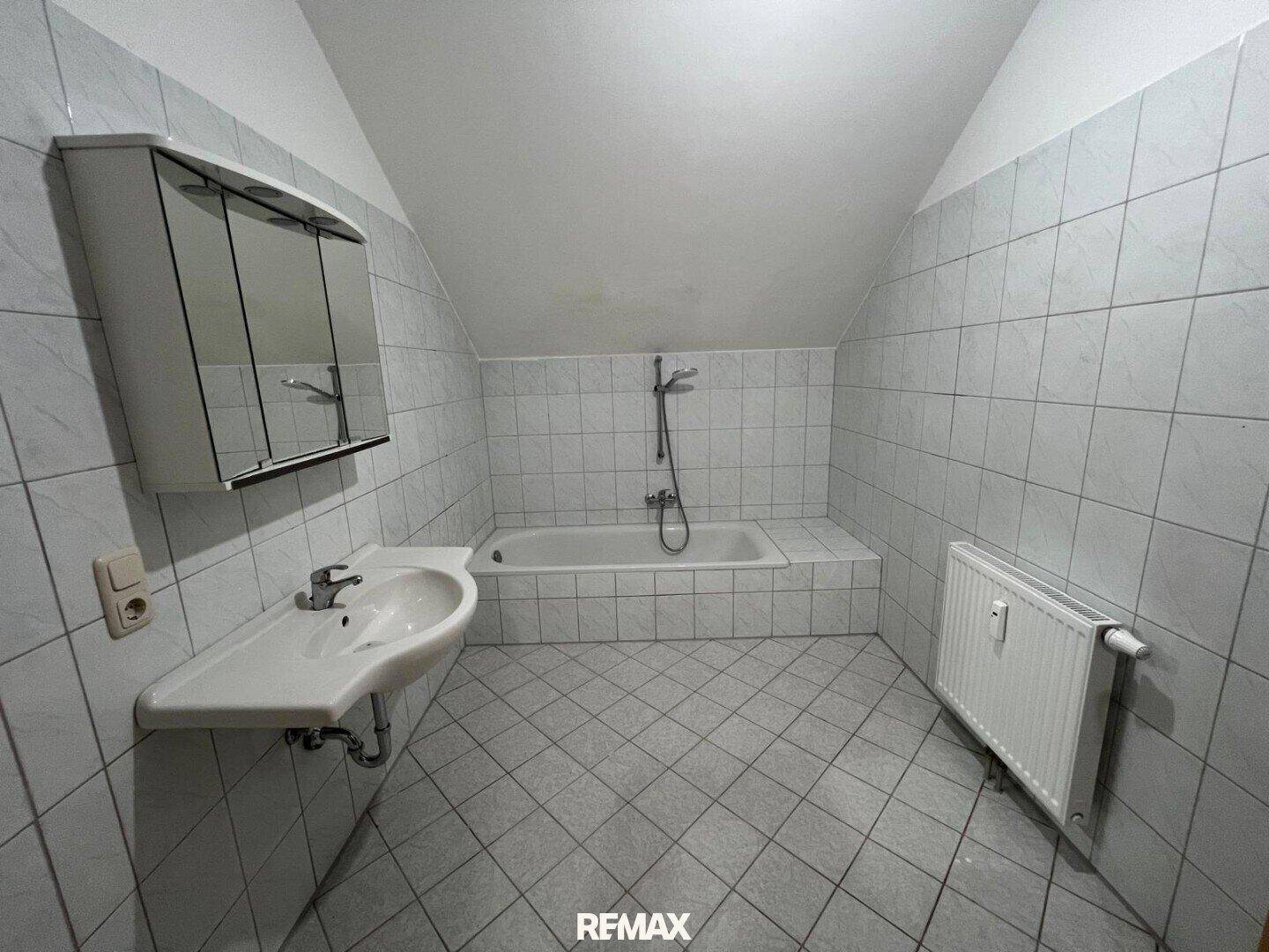 Badezimmer mit Badewanne, Waschbecken und Spiegelschrank unter einer Dachschräge.