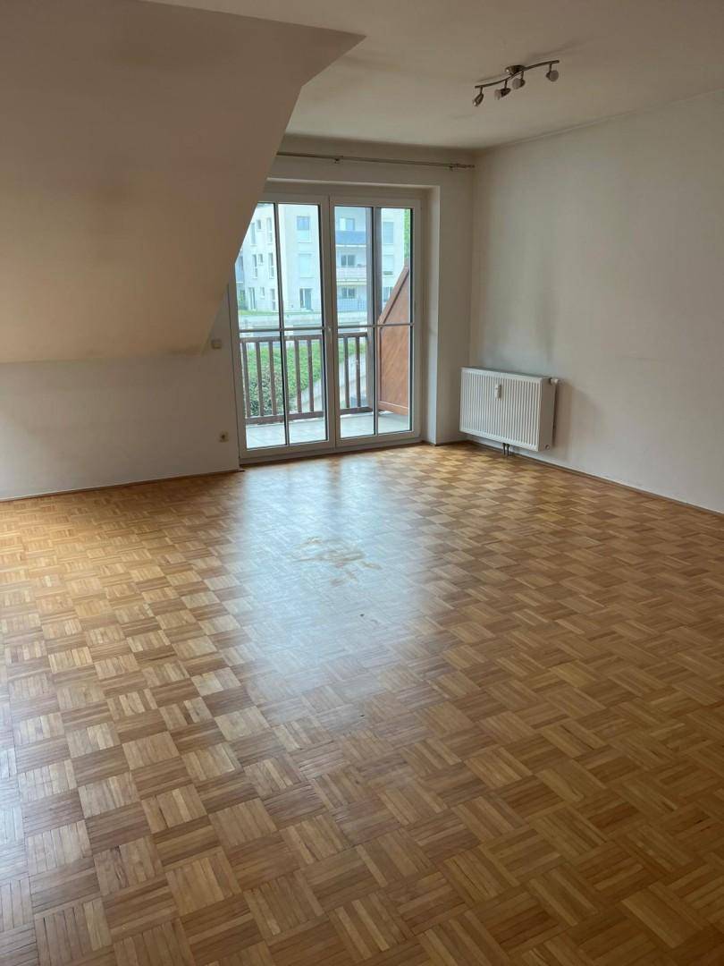Heller Raum mit Parkettboden, Dachschräge und großem Fenster mit Zugang zu einem Balkon.