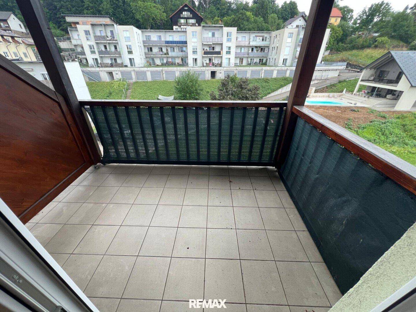 Balkon mit Fliesenboden und Holzelementen, bietet einen Blick auf die umliegenden Gebäude und den Pool.