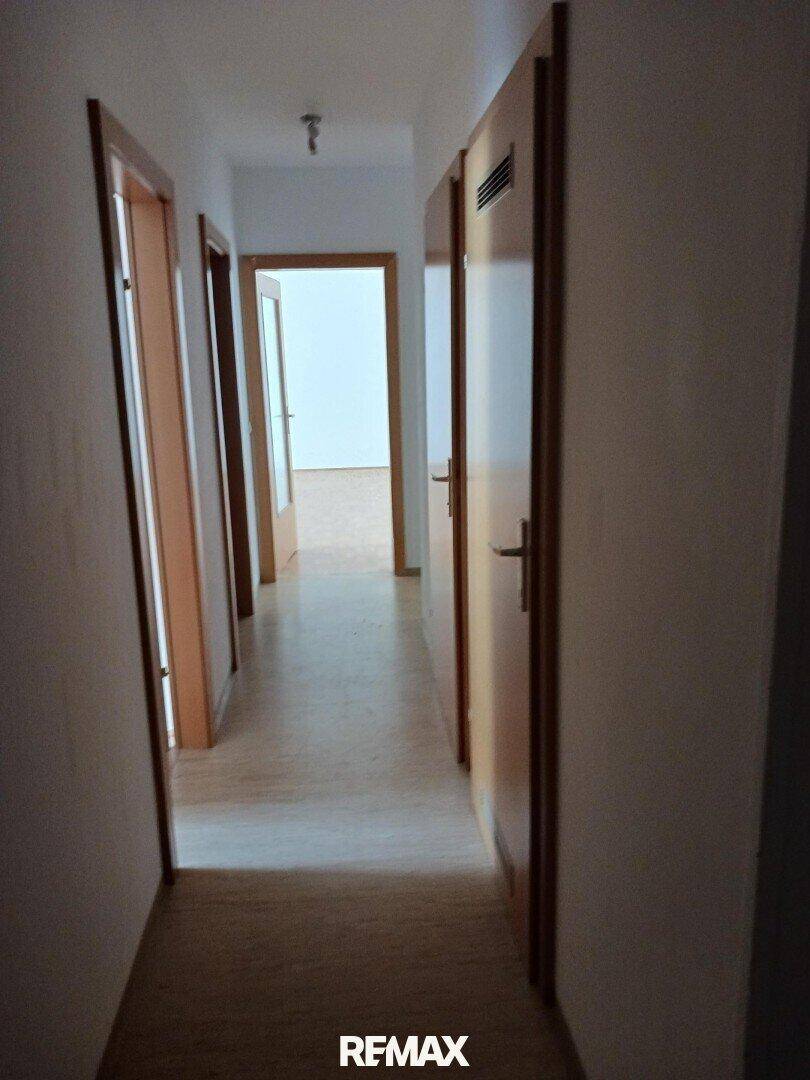 Langer Flur mit Holztüren und hellem Boden, der zu verschiedenen Räumen führt.