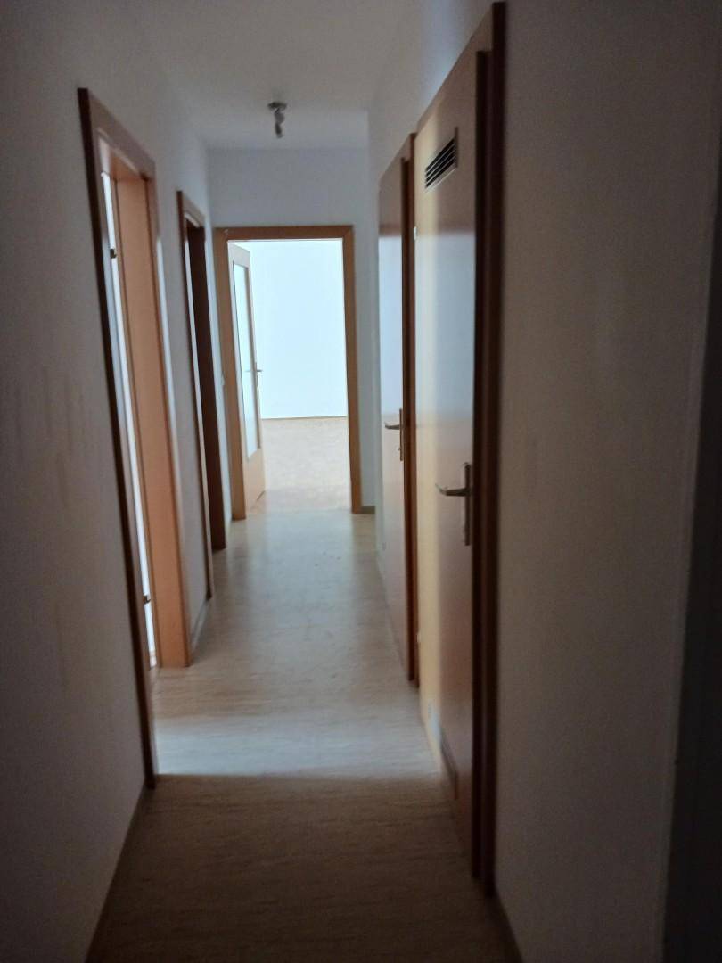 Langer Flur mit hellem Parkettboden und mehreren Holztüren, der verschiedene Räume der Wohnung verbindet.