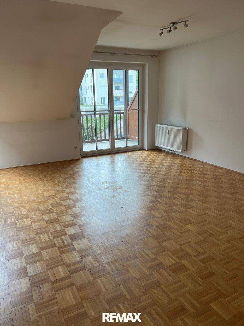 Heller Wohnbereich mit Parkettboden, Heizkörper und Zugang zu einem Balkon.