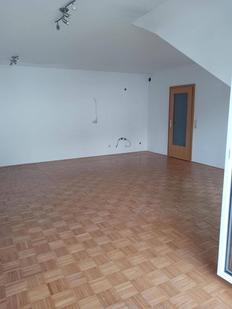 Geräumiger, leerer Raum mit Parkettboden und Dachschräge, ausgestattet mit einer Holztür mit Glaseinsatz.