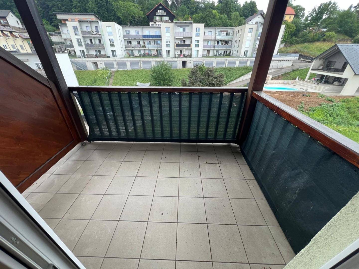 Balkon mit Fliesenboden und Holzbalken, bietet einen Ausblick auf die Nachbarschaft und einen Pool.
