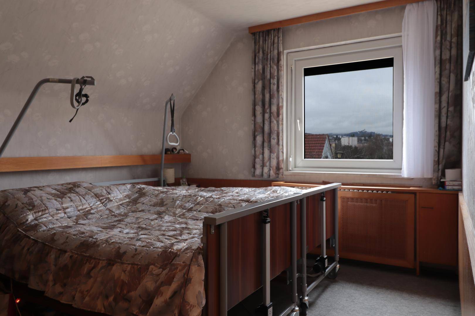 Schlafzimmer im Dachgeschoss mit schräger Decke, Fenster und weitem Blick über die Landschaft.