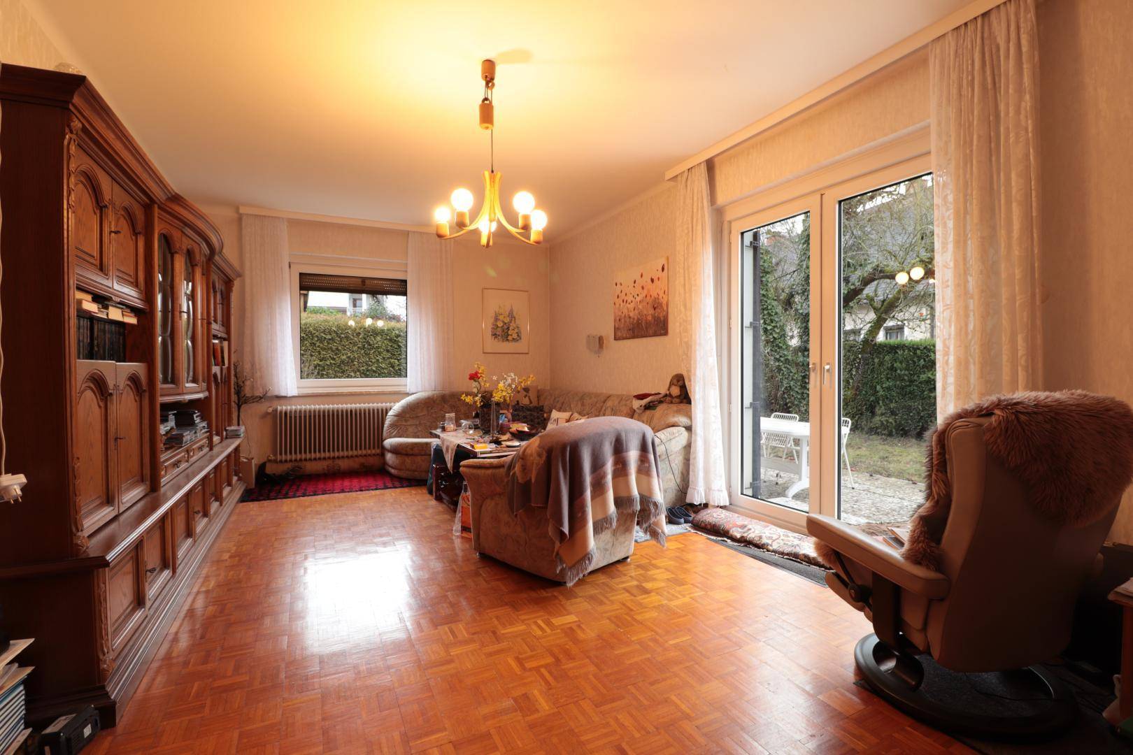 Helles Wohnzimmer mit Fischgrätparkett, großem Holzschrank und direktem Zugang zum Garten.