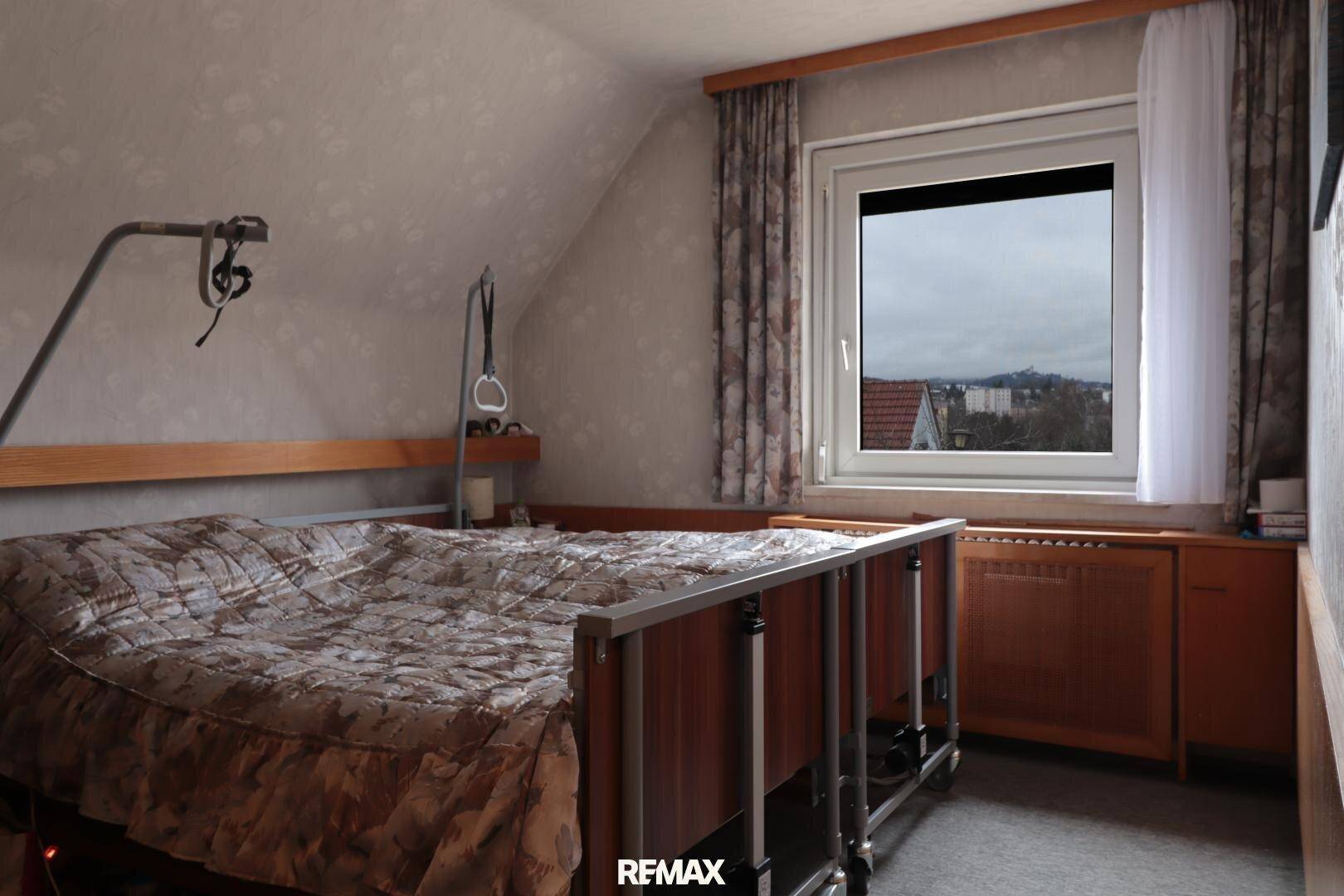 Schlafzimmer im Dachgeschoss mit schrägen Wänden, Fenster und Blick in die Ferne.