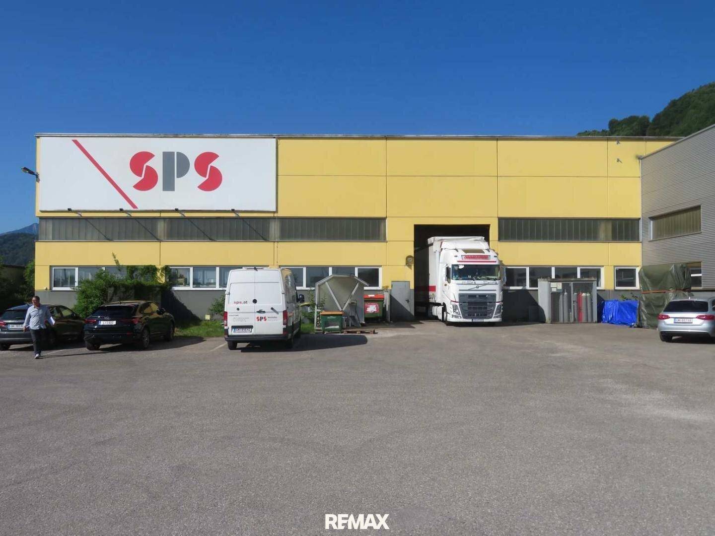 Gelbes Industriegebäude mit großem SPS-Logo und einem LKW, der in eine Ladebucht fährt.