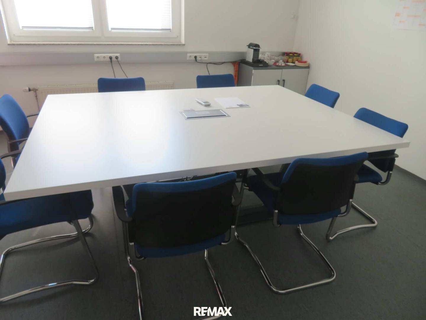 Besprechungsraum mit einem großen weißen Tisch und blauen Stühlen, ideal für Teammeetings.