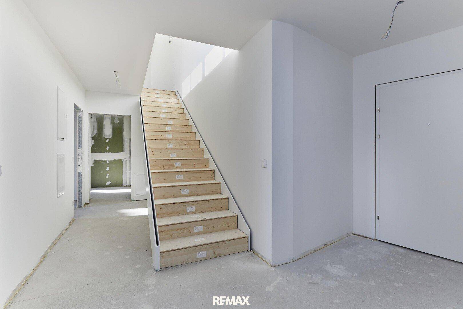 Unfertiger Flur mit Holztreppe und viel Tageslicht von einem Oberlicht.