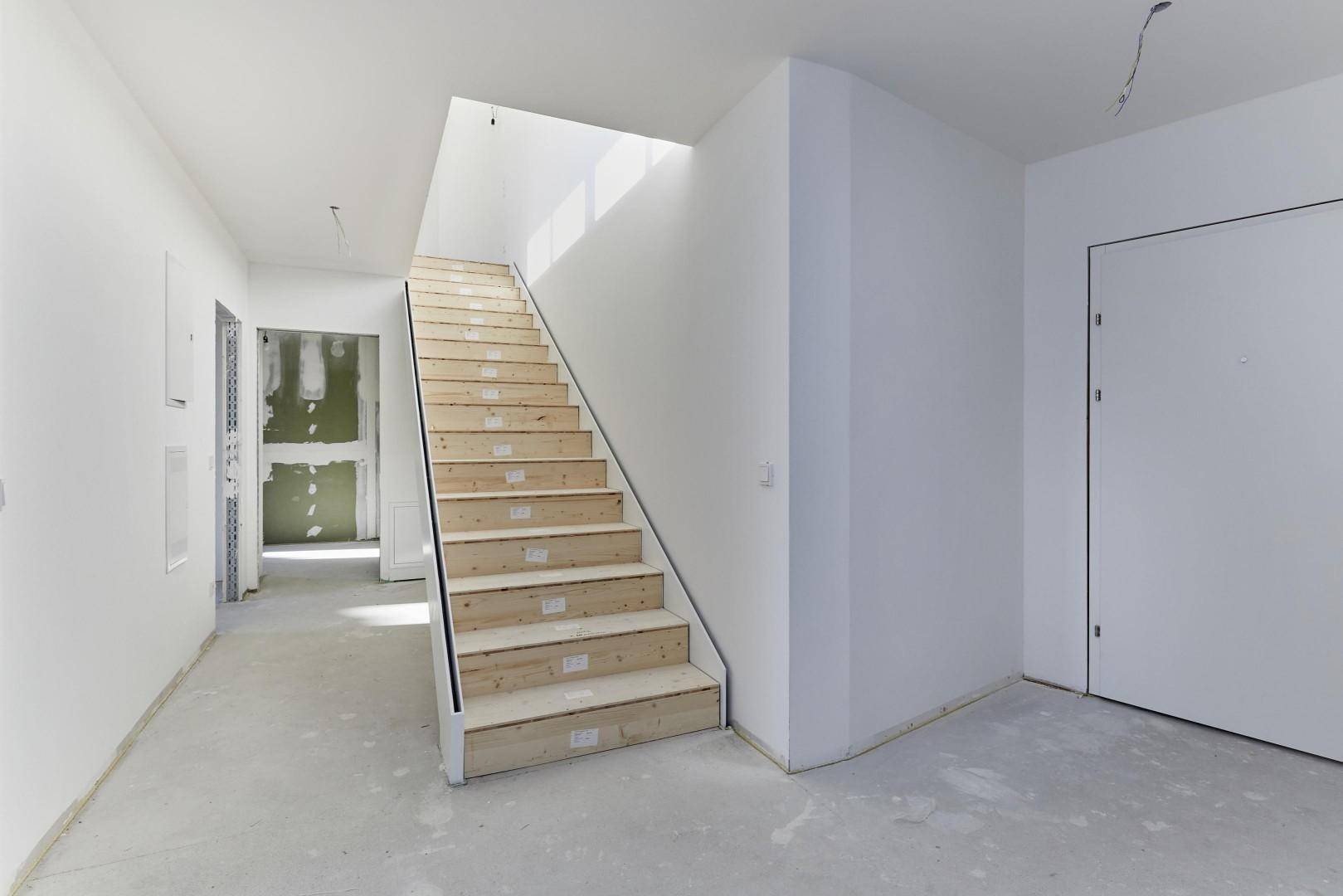 Flur im Rohbau mit einer Holztreppe, die in die oberen Stockwerke führt.