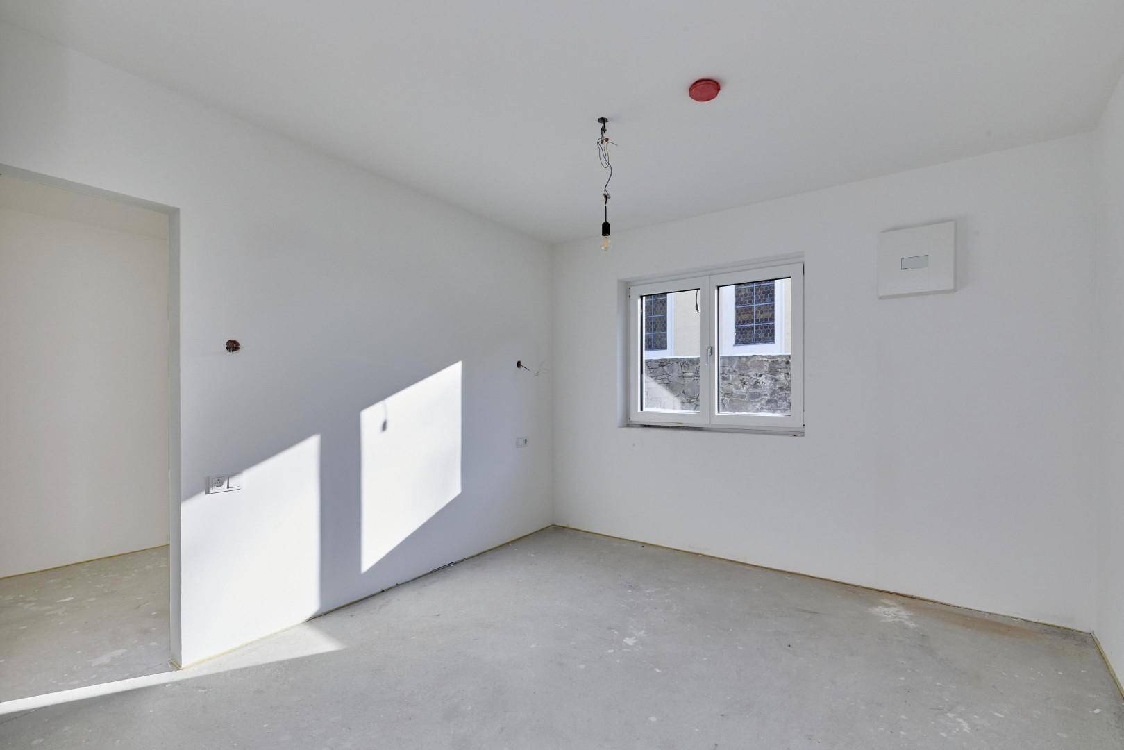 Leerer Raum im Rohbau mit einem Fenster, bereit für den Innenausbau.