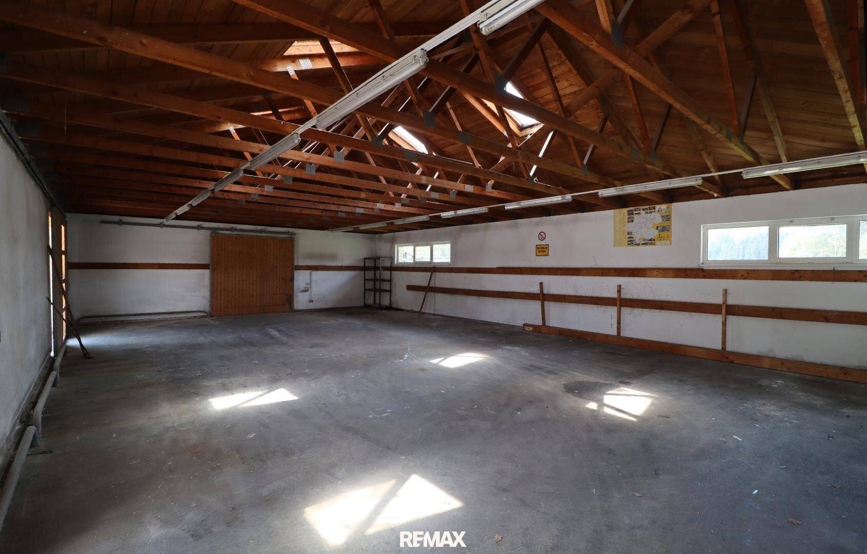Großer Lagerraum mit sichtbaren Holzbalken an der Decke, Betonboden und natürlichem Lichteinfall durch Fenster.