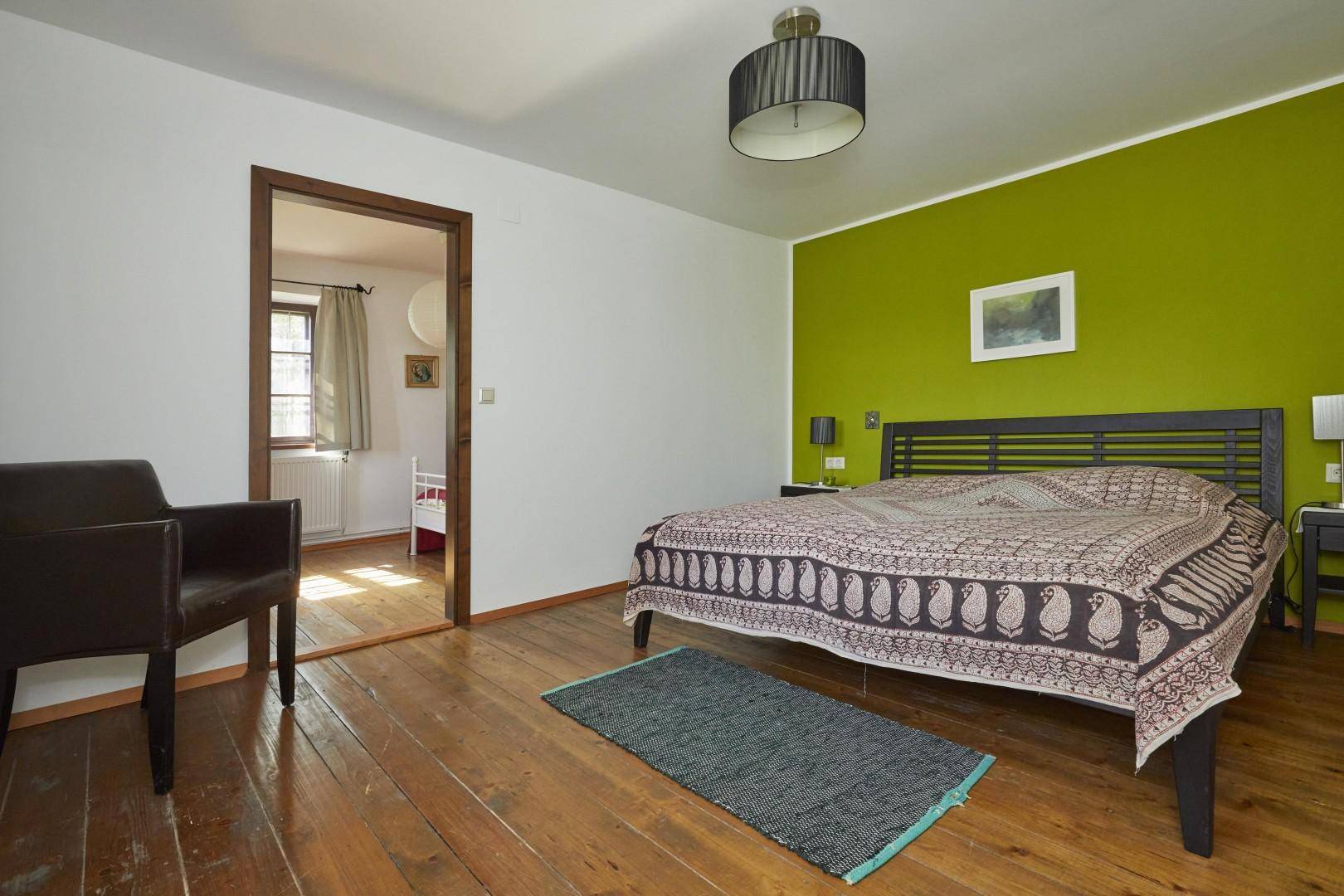 Modernes Schlafzimmer mit grüner Akzentwand, Holzdielenboden und schlichtem Design.