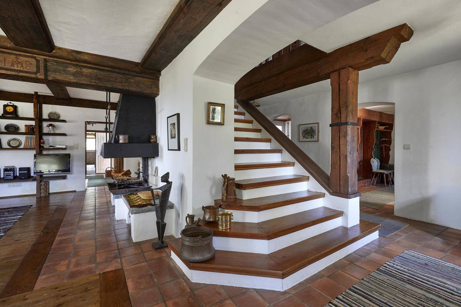Geräumiger Flur mit rustikaler Holztreppe, großem Kamin und Terrakotta-Bodenfliesen.
