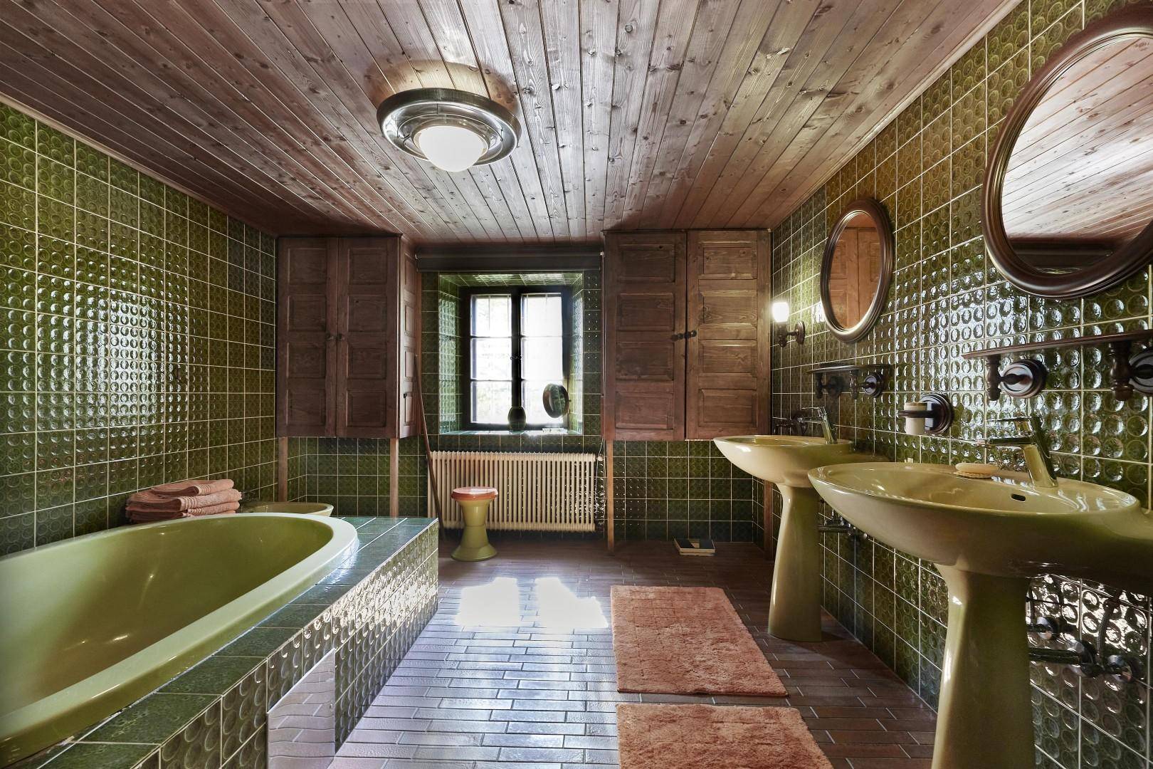 Badezimmer mit grünen Fliesen, Holzdecke, zwei Waschbecken und einer Badewanne im Vintage-Stil.