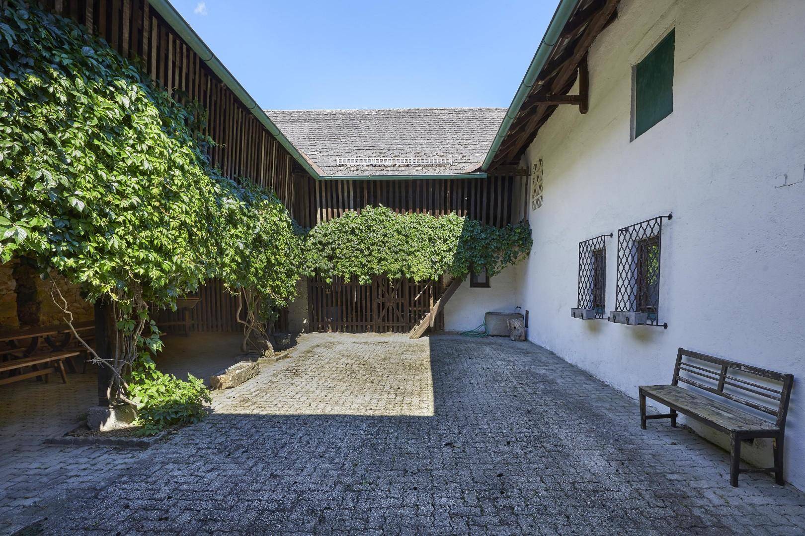 Idyllischer Innenhof mit Kopfsteinpflaster, bewachsenen Wänden und einer rustikalen Holzbank.