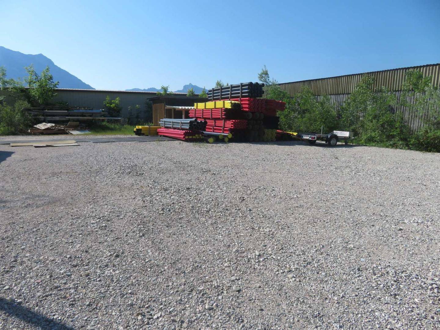 Großer Schotterplatz im Freien mit gestapelten Materialien und einer grünen Umgebung mit Bergblick im Hintergrund.