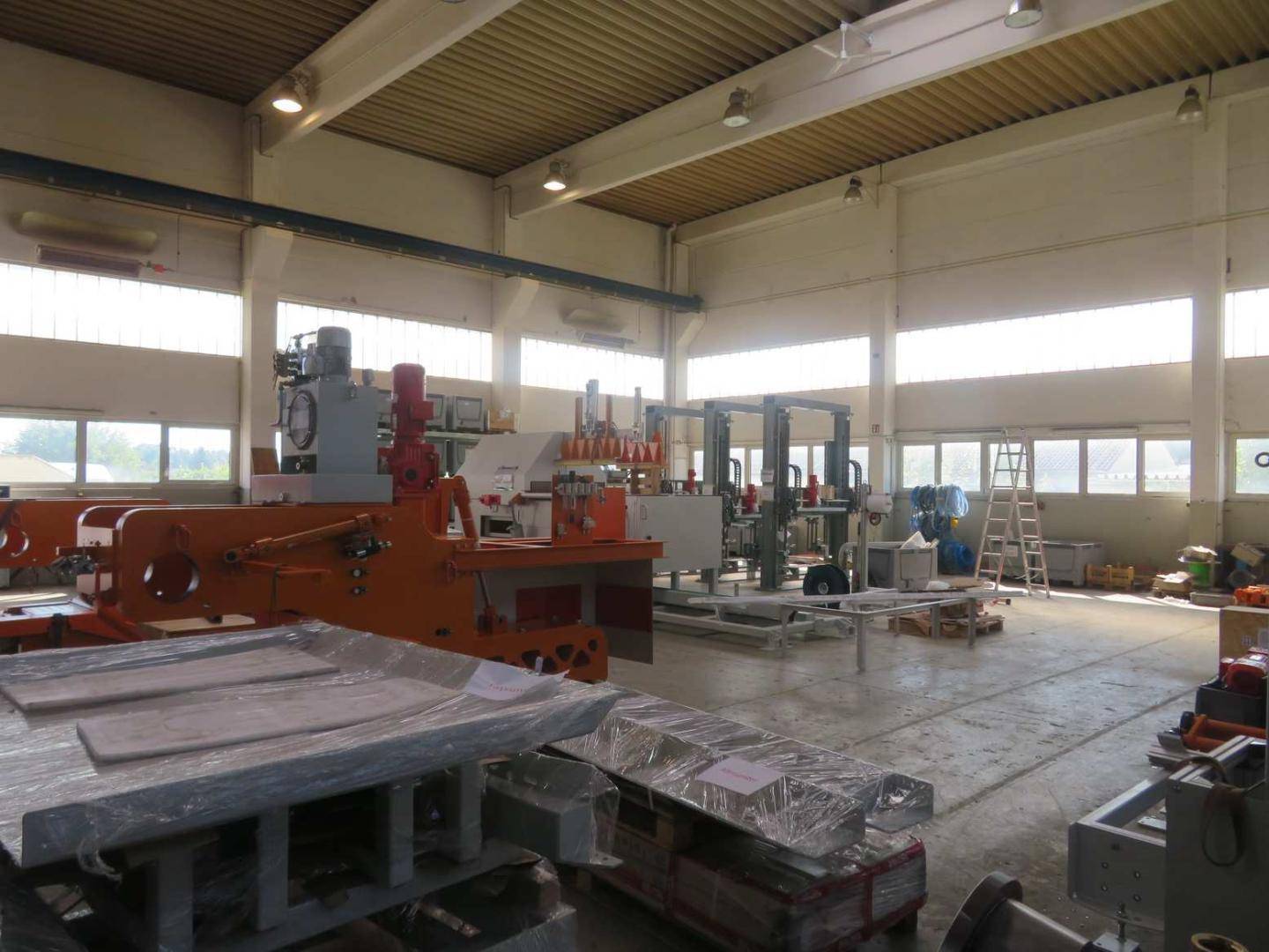 Helle Produktionshalle mit großen Fenstern, Maschinen und einem Betonboden, der viel Arbeitsfläche bietet.
