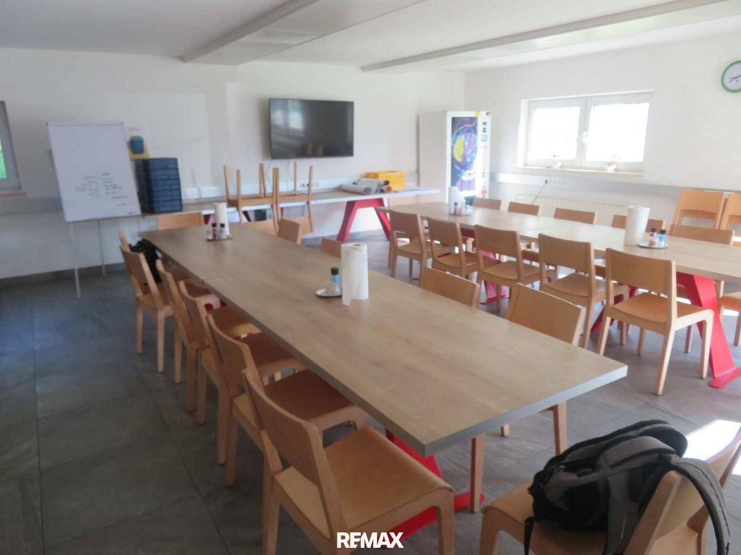 Großer Pausenraum oder Kantine mit mehreren langen Tischen und Stühlen, ideal für Mitarbeiter.