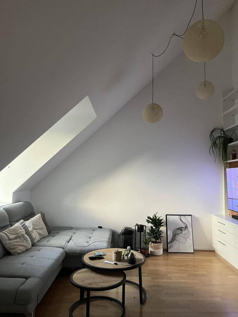 Gemütliches Wohnzimmer im Dachgeschoss mit schräger Decke, Ecksofa und Holzboden.