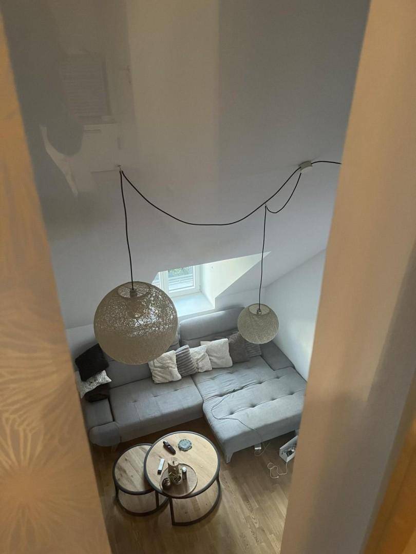 Blick von oben auf ein gemütliches Wohnzimmer im Dachgeschoss mit schräger Decke und Ecksofa.