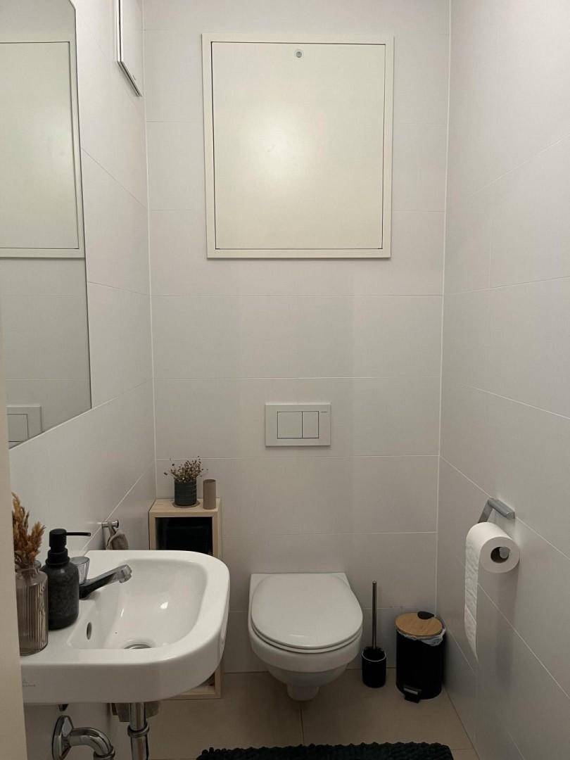 Kleines Gäste-WC mit wandmontierter Toilette, Waschbecken und weißen Fliesen.