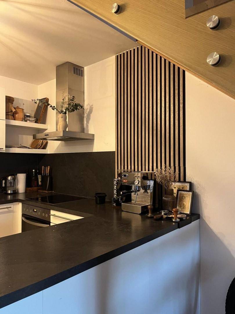 Helle Küche mit dunkler Arbeitsplatte, integriertem Backofen und einer Holzlamellenwand.