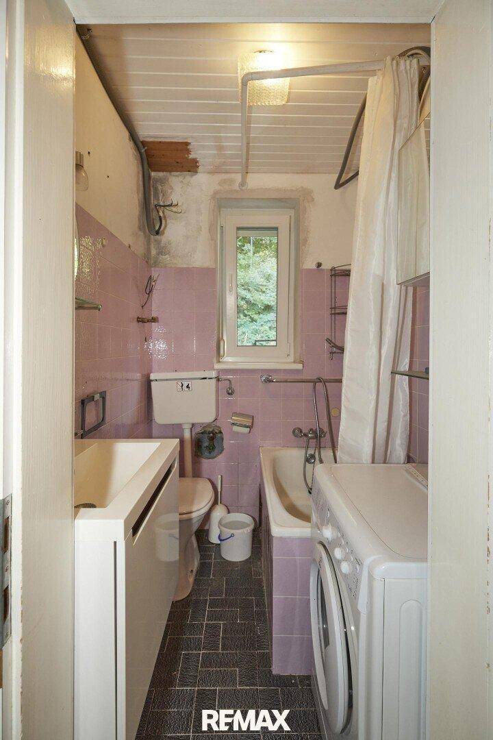 Kleines Badezimmer mit rosa Fliesen, Badewanne, WC und Waschmaschine, ausgestattet mit Fenster.