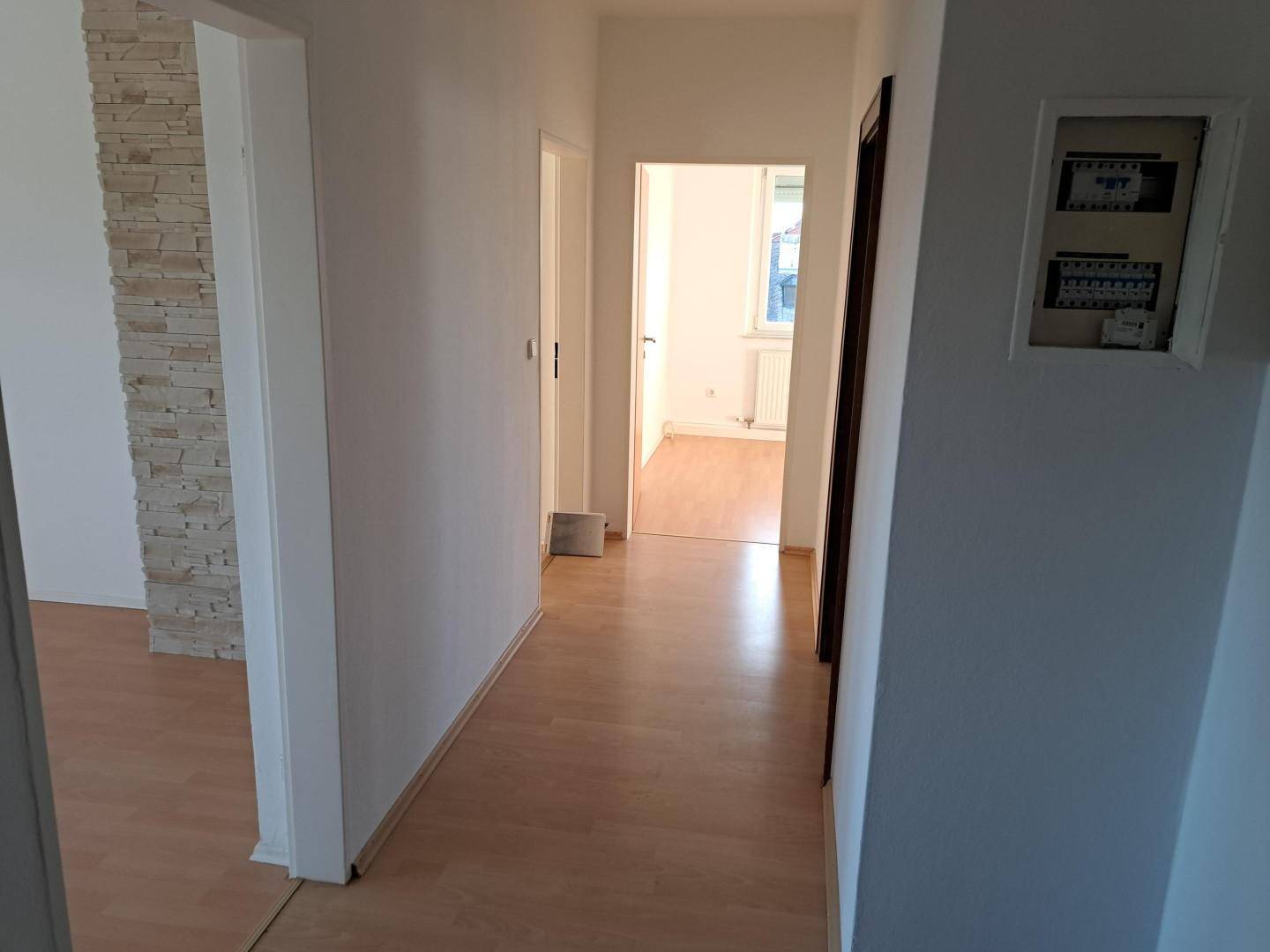 Langer Flur mit Laminatboden, weiß gestrichenen Wänden und dekorativer Steinwand im Hintergrund.
